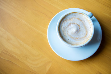 hot coffee cappuccino cup with milk foam on wood table background. Drinken latte art coffee on wooden table.Cup of cappuccino on the table, coffee shop background.
