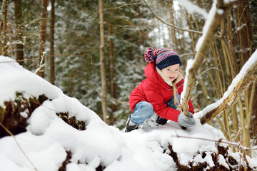 Adorable little girl having fun in beautiful winter forest. Happy child playing in a snow.