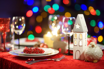 Beautiful table setting for Christmas party or New Year celebration at home. Cozy room with a fireplace and Christmas tree in a background.