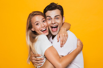 Loving couple standing isolated over yellow wall background hugging.