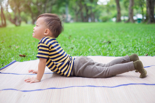 Cute little Asian 30 months / 2 year old toddler baby boy child practices yoga in Cobra Pose and meditating outdoors on nature in summer time, Healthy lifestyle, Yoga for Kids to improve concentration