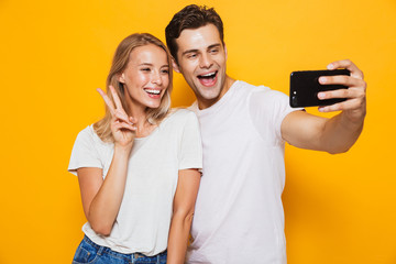 Young loving couple standing isolated over yellow wall background take a selfie by mobile phone.