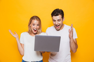 Happy excited young loving couple isolated over yellow wall background using laptop computer.