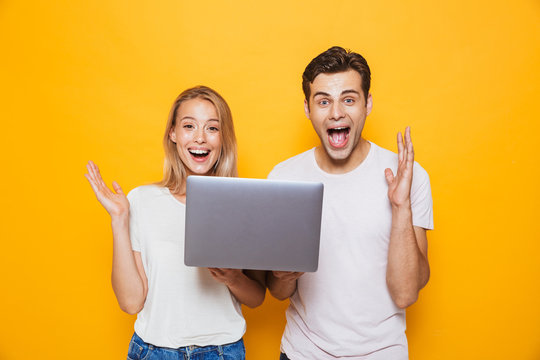 Happy excited young loving couple isolated over yellow wall background using laptop computer.