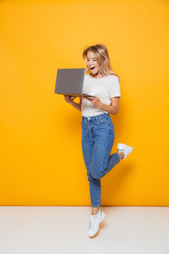 Excited young woman jumping isolated over yellow wall background using laptop computer.