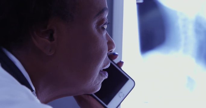 Senior female African doctor discussing x-ray with colleague over cell phone. Mid aged black MD talking on mobile phone with patient about x ray