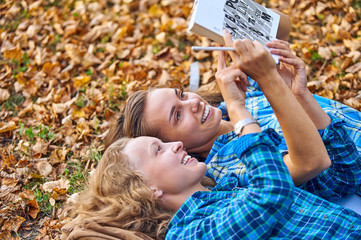Obraz premium Two beautiful women lying on leaves and reading books in autumn park. Education, friendship lifestyle concept