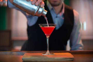 Barman pours a Cosmopolitan cocktail from a shaker into a glass - obrazy, fototapety, plakaty