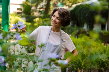 Woman gardener standing over plants in greenhouse water flowers