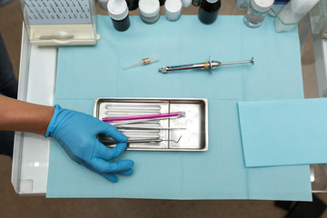 the dentist's hand in the blue glove takes the tool from the tray with tools.