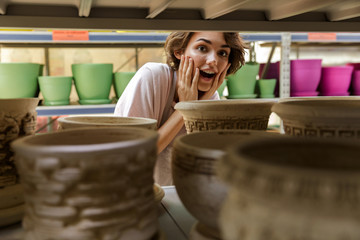 Shocked cute woman gardener standing in greenhouse choosing vase pot for plants.