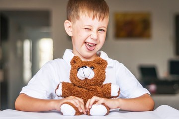 Funny and naughty Caucasian child with a toy teddy bear. Kid showing tongue. Happy childhood concept.