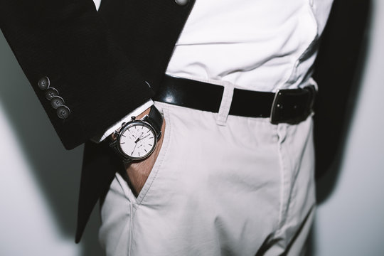 Closeup fashion image of luxury watch on wrist of man.body detail of a business man.Man's hand in beige pants pocket closeup at white background.Man wearing black jacket and white shirt.Not isolated