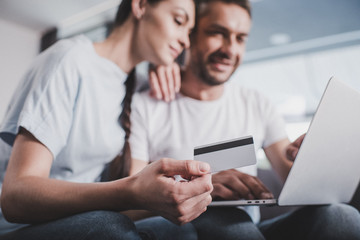 selective focus of smiling couple with laptop doing online shopping by credit card at home