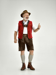 Portrait of Oktoberfest senior man in hat, wearing a traditional Bavarian clothes standing at full-length at studio. The celebration, oktoberfest, festival concept
