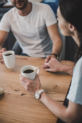 partial view of couple drinking coffee and holding hands at table