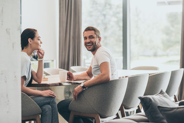 laughing adult man with coffee cup sitting at table with girlfriend at home