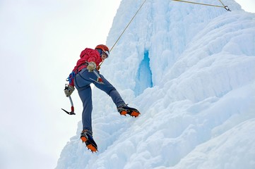 Alpinist woman with  ice tools axe in orange helmet climbing a l