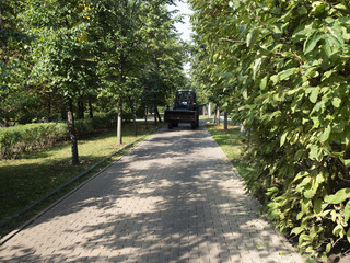 Sunny autumn day. Tractor rides on a brick walkway in the garden, with beautiful green trees