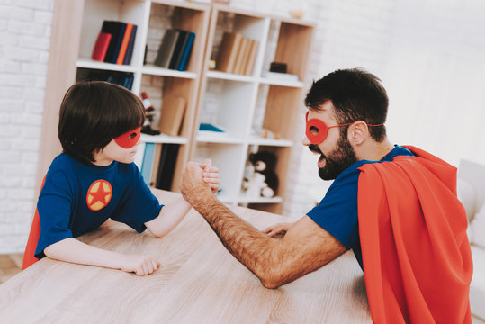 Dad And Son Arm Wrestling In Superhero Suits.