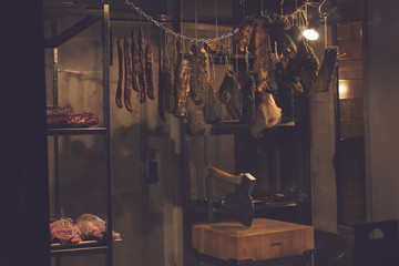 Meat products in a dimly lit dry-aging chamber in a butcher's shop.
