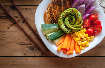 Buddha bowl with roasted chicken and fresh vegetables on wooden background, top view