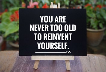 Motivational and inspirational quote - ‘You are never too old to reinvent yourself’ written on a blackboard. Blurred vintage styled background.
