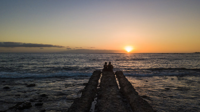 Romantic Aged Senior Couple Sitting Together At The End Of The Dock Looking The Sunset And Enjoying Love And Relationship Foreverness. Life And Enjoy The Nature Concept For Two Caucasian Adults 