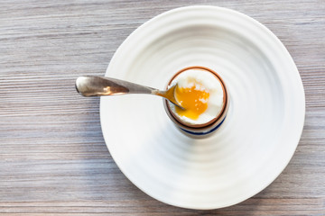 soft-boiled brown egg with spoon on plate on gray