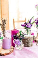 Fototapeta na wymiar Purple lavender wedding. Table decor with dry lavender, green and white flowers. Candles, wooden rustic vases, Glass jars, lace bottles, sawed wood.