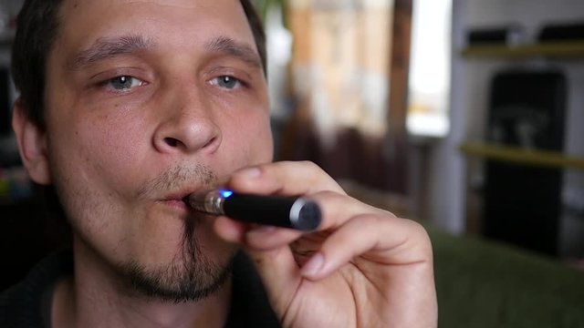 Man smoking electronic cigarette in attempt to breath out smoke rings