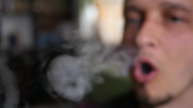 Man smoking Electronic Cigarette at home closeup breathing out a smoke rings