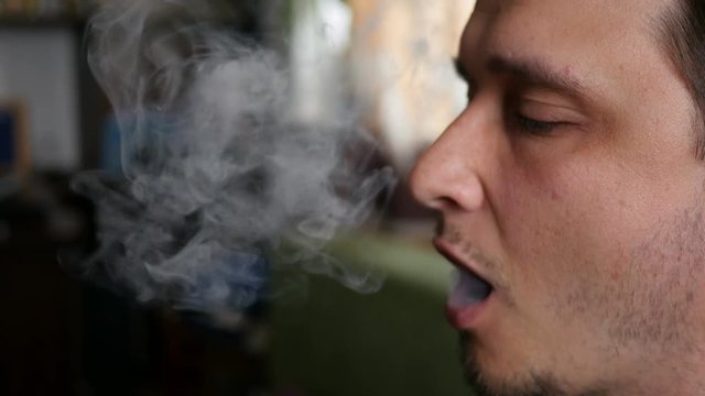 Man smokes electronic cigarette at home exhaling smoke