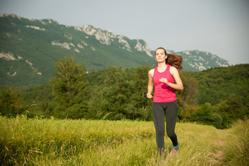 Fototapeta na wymiar Beautiful young woman workout outdoor runs across meadow in early summer