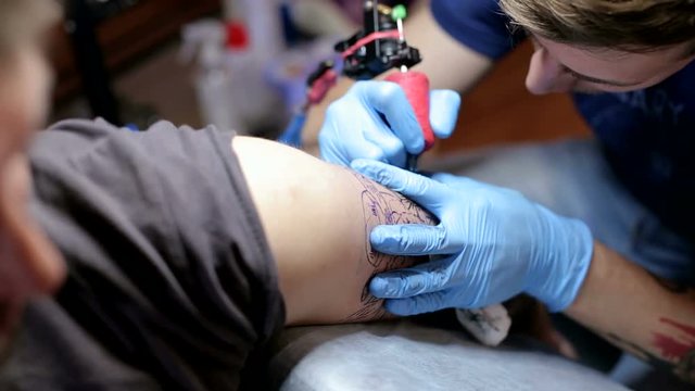 Close-up of a tattoo artist doing a tattoo on a man's arm in the salon. Professional tattooist doing tattooing in studio. Skin art close-up, male beauty salon.