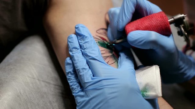 Professional tattoo artist make color tattoo on man's arm, he fill the tattoo with green ink. The process of tattooing on the hand.