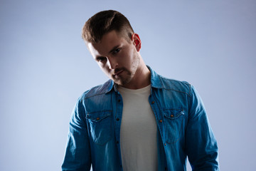 Casual style. Serious handsome man wearing a jeans jacket while standing against the blue background