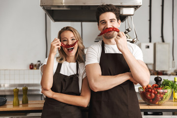 Friends loving couple chefs on the kitchen having fun with pepper as a moustache.