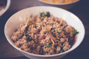 Sliced grilled pork salad with Packs of steamed sticky rice and Basil branches as background on wooden table (Thai food) Vintage tone
