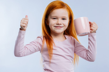 Great mood. Cheerful positive girl holding a cup while showing the OK sign