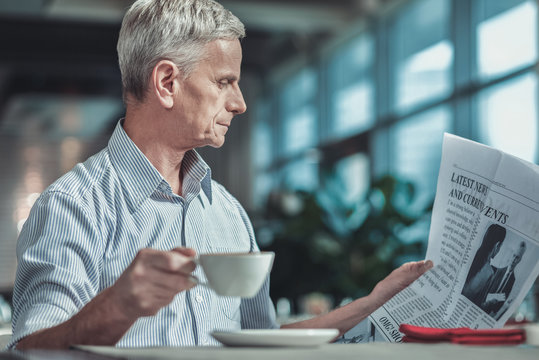Have a look. Profile photo of concentrated man that holding cup and looking at newspaper