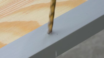 Closeup of a drill bit drilling a hole in the aluminum straight edge profile. Copy space.