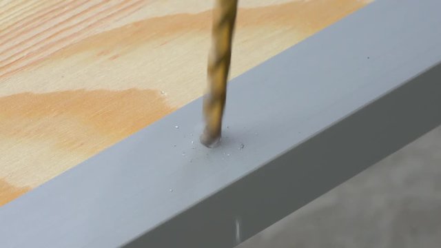 Closeup of a drill bit drilling a hole in the aluminum straight edge profile. Copy space.