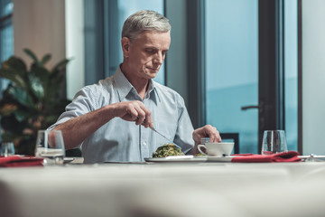 Fresh food. Concentrated male person bowing head while trying new dish