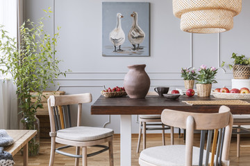 Wooden chairs at table with flowers in natural dining room interior with poster and lamp. Real photo