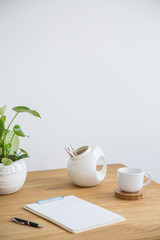 Notes, pen, mug and plant on a wooden desk with an empty wall in the background. Place your poster