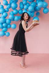 young girl holding birthday cake with candles in pink studio room with shiny blue balls decor