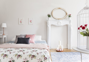 A bright bedroom interior with an English style decor. A bed and a fireplace mantel against a wall. Real photo.