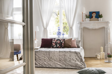 A view from a different room into a cozy chic bedroom interior with a big bed with pillows and a...