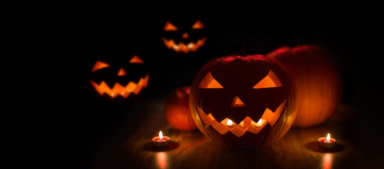 halloween and holidays concept - many spooky carved pumpkin jack-o-lanterns with candles in darkness